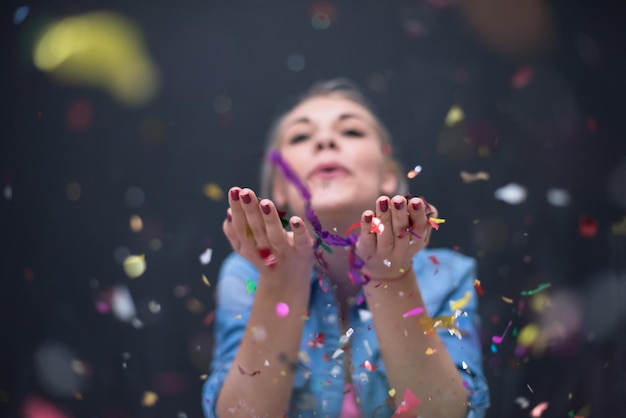 Bela jovem comemorando ano novo e festa de natal enquanto sopra decorações de confete para a câmera