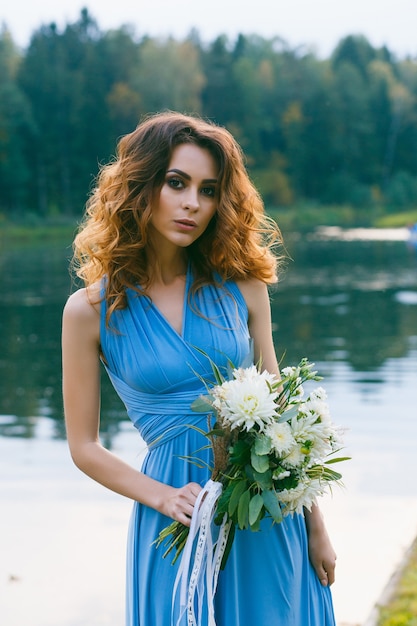 Bela jovem dama de honra posando perto do lago no dia do casamento