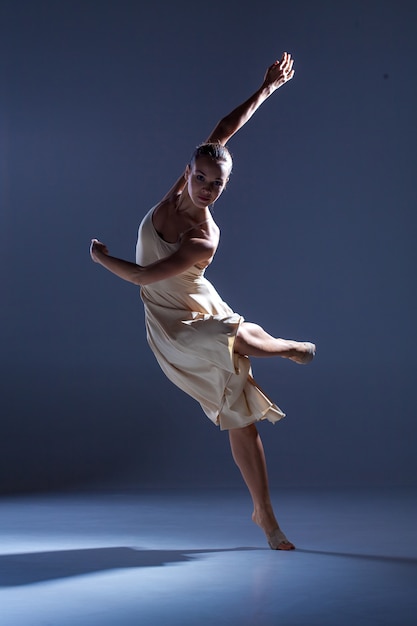 Bela jovem dançarina em um vestido bege dançando no fundo cinza do estúdio