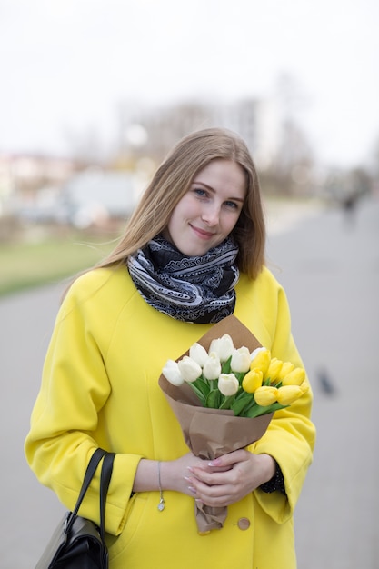 Bela jovem de casaco amarelo com flores brancas e amarelas