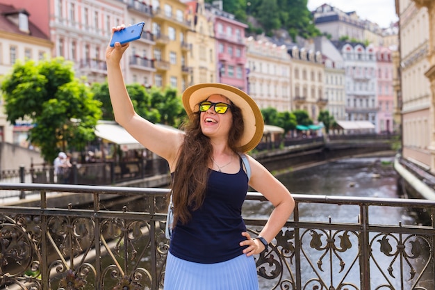 Bela jovem de óculos, caminhando na cidade europeia e fazendo selfie