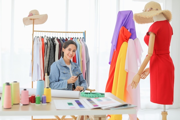 Bela jovem designer de moda feminina usando smartphone e sorria. Ela está feliz com seu vestido acabado e compartilha com suas amigas.