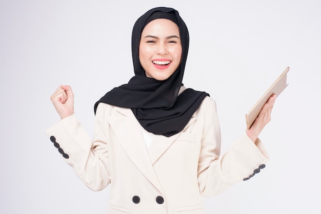 Bela jovem empresária muçulmana de terno segurando um tablet sobre o fundo branco do Studio