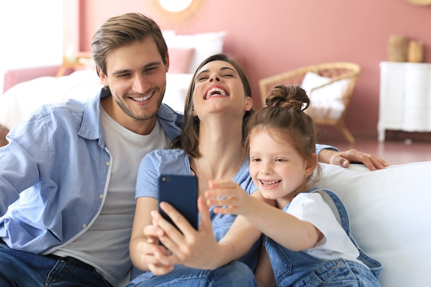 Foto bela jovem família com criança tomando uma selfie com um smartphone em casa no sofá.