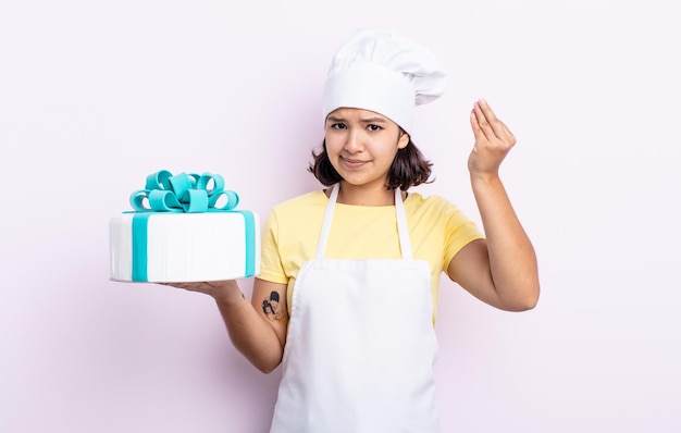 Bela jovem fazendo capice ou gesto de dinheiro, dizendo para você pagar. chef cozinhando um bolo