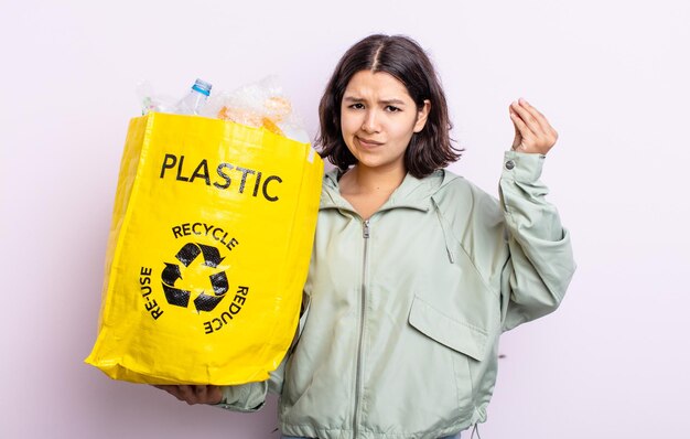 Bela jovem fazendo gesto capice ou dinheiro, dizendo para você pagar. conceito de reciclagem de plástico