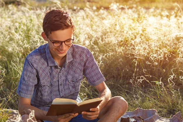 Bela jovem feliz com óculos ao ar livre, lendo um livro em um dia ensolarado