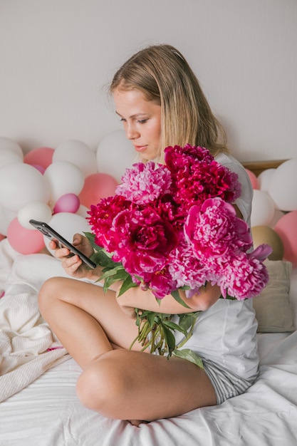 bela jovem feliz em casa, na cama, segurando flores, tire uma selfie pelo celular