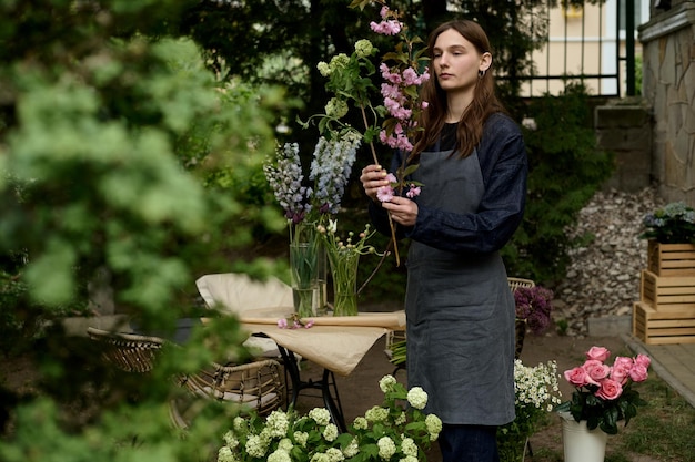 Bela jovem florista em um terraço verde faz um buquê