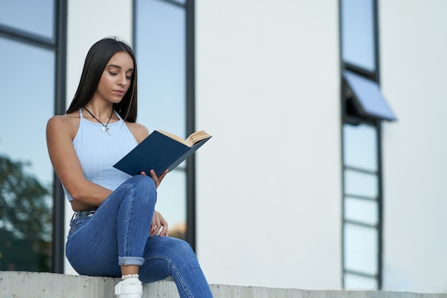 Foto bela jovem lendo um livro fora da faculdade