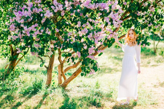 Bela jovem loira de vestido branco, posando no parque ensolarado de verão.