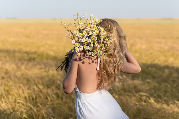 Bela jovem loira em um campo de trigo em um vestido branco no verão