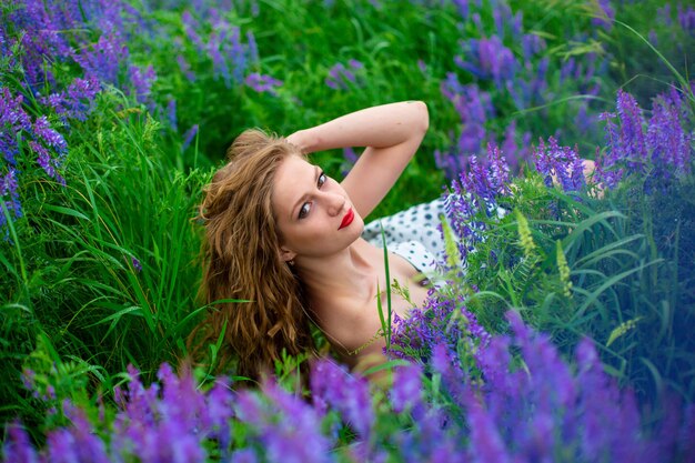 Bela jovem loira em um campo verde entre flores silvestres roxas. garota linda de vida selvagem.