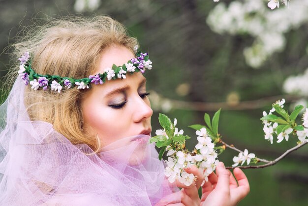 bela jovem loira na coroa de flores florescendo árvores na primavera