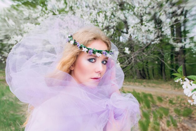 bela jovem loira na coroa de flores florescendo árvores na primavera