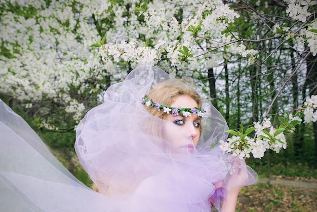 bela jovem loira na coroa de flores florescendo árvores na primavera