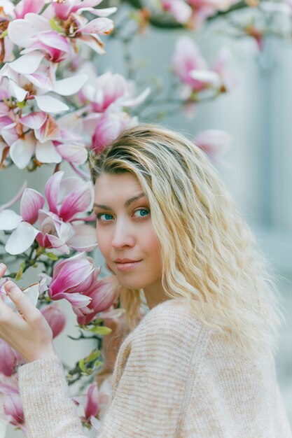 Bela jovem loira perto de uma magnólia em flor