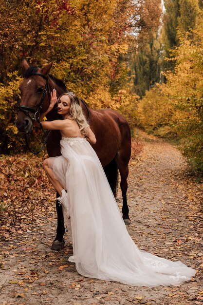 Bela jovem loira posando em um parque no outono com um cavalo