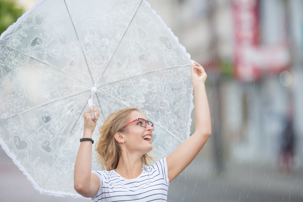 Bela jovem loira segurando guarda-chuva na chuva de verão.