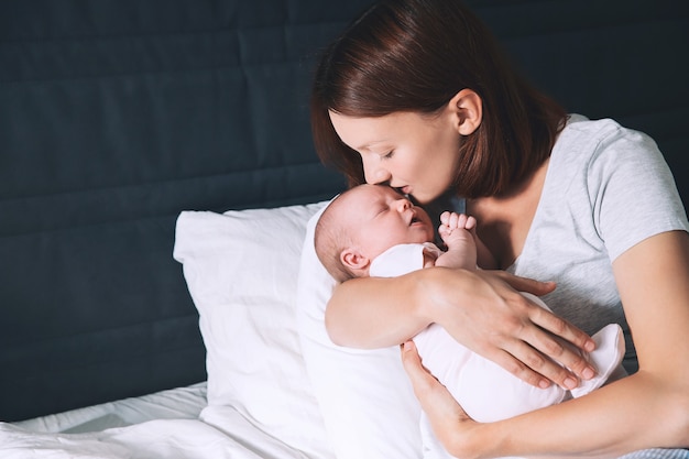 Bela jovem mãe beijando seu bebê recém-nascido Bebê dormindo nas mãos de sua amorosa mãe