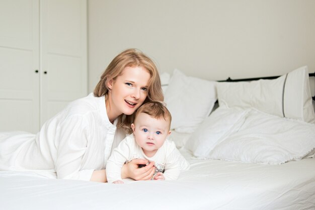 Bela jovem mãe com seu filho na cama. Manhã engraçada e sorridente. quarto branco