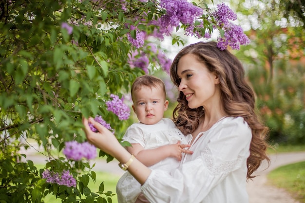 Bela jovem mãe e filha perto do florescimento lilás. Primavera.