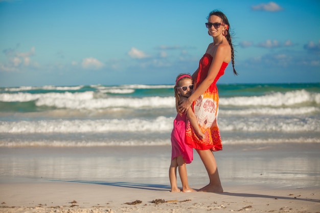 Bela jovem mãe e sua filha andando na praia tropical