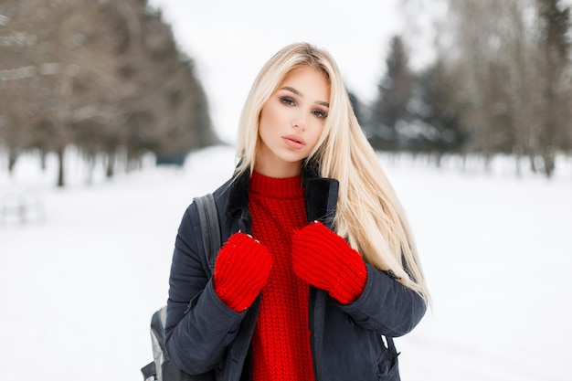 Bela jovem modelo mulher com um elegante casaco de inverno e um suéter vermelho de malha ao ar livre em um dia nevado de inverno