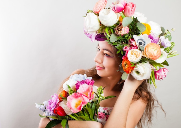 Bela jovem modelo sorridente com flores brilhantes na cabeça sobre parede branca Mulher com maquiagem perfeita