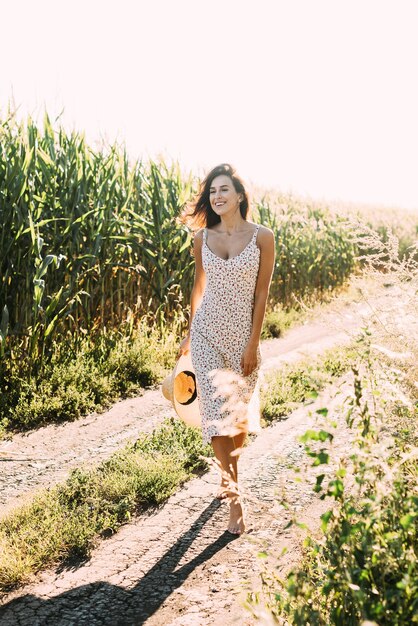 Bela jovem morena com uma roupa de verão elegante e chapéu de palha sob os raios do sol na natureza