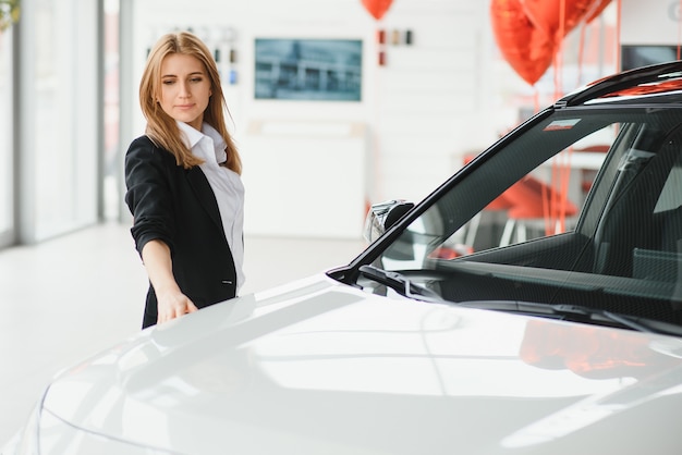 Bela jovem mostrando seu amor por um carro em um showroom de carros