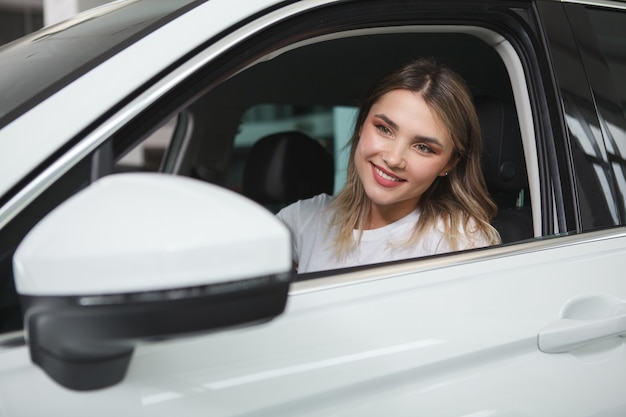 Bela jovem motorista do sexo feminino olhando no espelho lateral, sentada em um carro