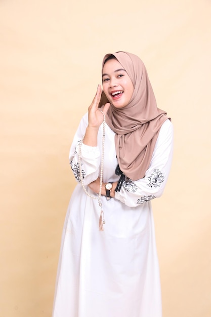Bela jovem muçulmana asiática vestindo um hijab carregando contas de oração à esquerda sorrindo alegremente