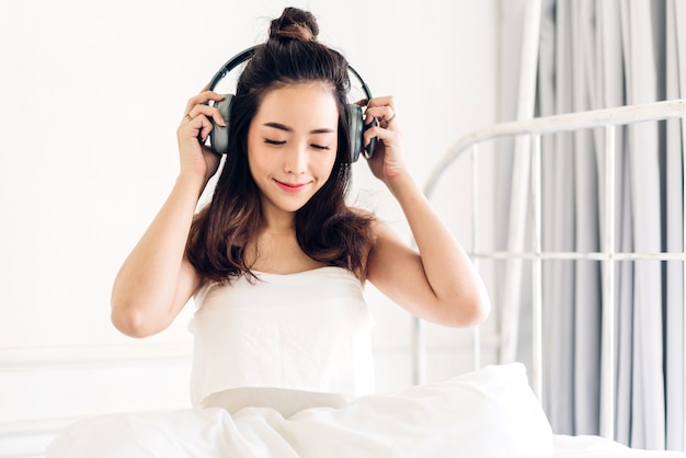 Bela jovem mulher asiática relaxante ouvindo música com fones de ouvido na cama