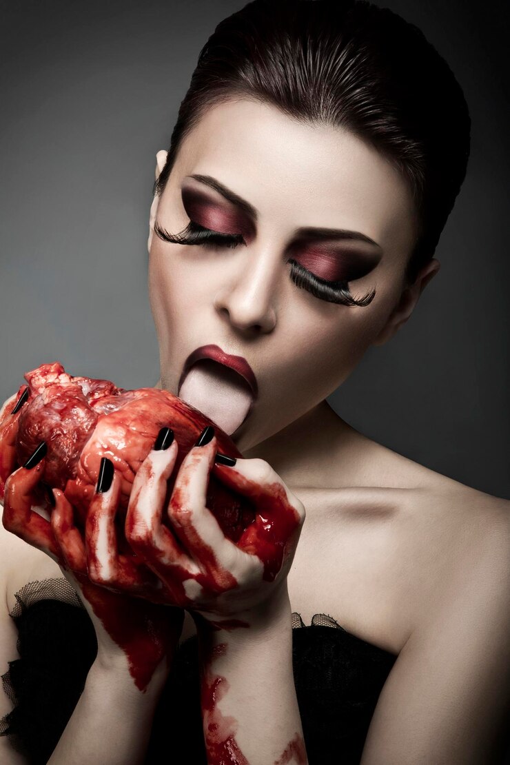 Foto bela jovem mulher lambendo sangue do coração humano contra um fundo cinzento