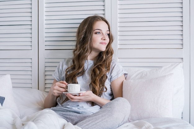 Bela jovem na cama no quarto tomando café da manhã