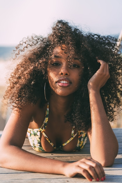 Bela jovem negra deitada em uma ponte de madeira na praia