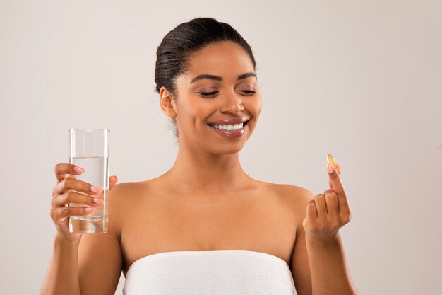 Bela jovem negra tomando pílula de beleza fundo cinza