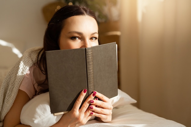 Bela jovem no quarto na cama com um livro