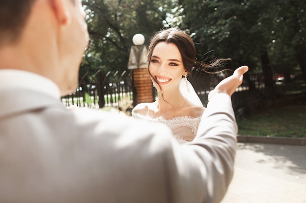 Bela jovem noiva elegante vestido branco, sorrindo encontra seu noivo no parque