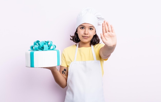 Bela jovem olhando sério mostrando a palma da mão aberta, fazendo gesto de parada. chef cozinhando um bolo