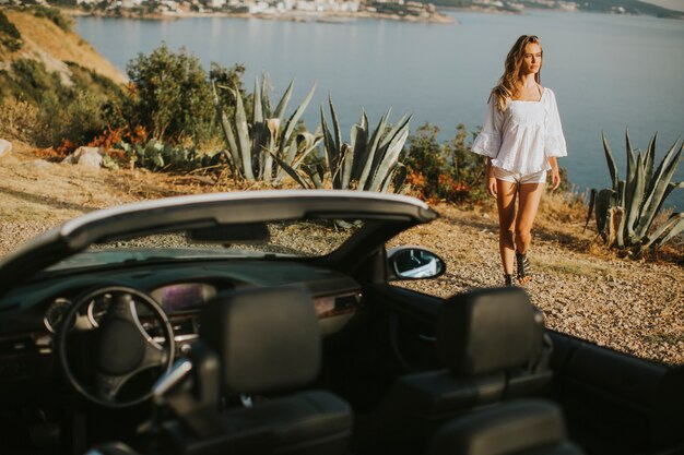 Bela jovem pelo carro cabriolet branco à beira-mar