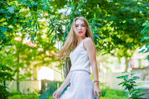 Bela jovem posando ao ar livre, usando um vestido branco elegante. Estilo de verão.