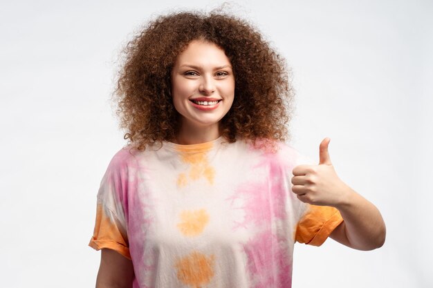 Foto bela jovem positiva com cabelo encaracolado mostrando o dedo para cima ok sinal olhando para a câmera
