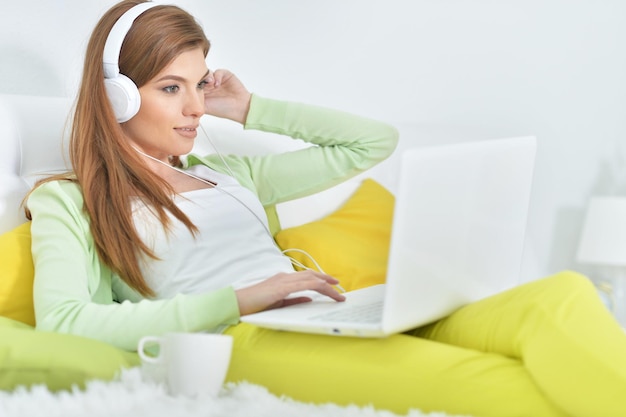 Bela jovem relaxando na cama em casa, usando laptop