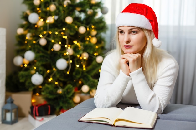 Bela jovem rezando em frente à árvore de Natal decorada