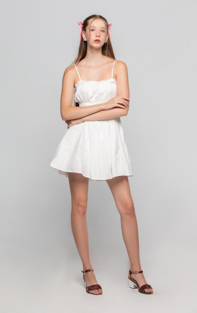 Bela jovem romântica em um vestido curto branco posando no estúdio em um fundo cinza