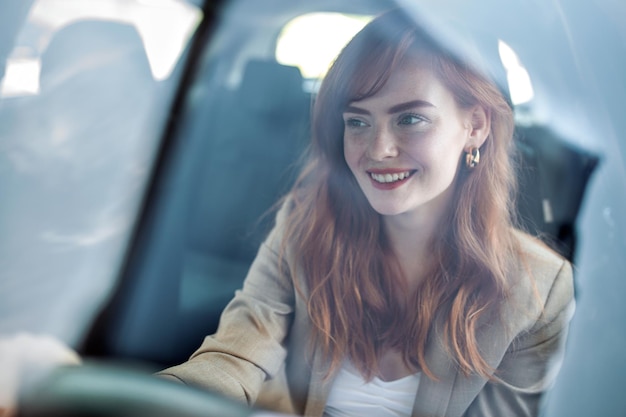 Bela jovem ruiva sorridente atrás do volante dirigindo o carro