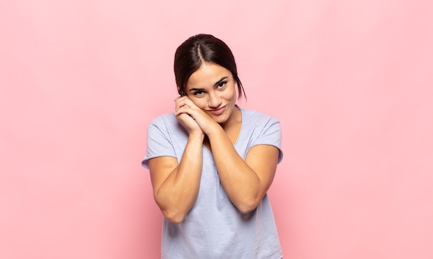 Bela jovem se sentindo apaixonada e bonita, adorável e feliz, sorrindo romanticamente com as mãos ao lado do rosto