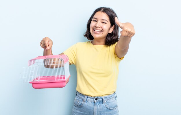 Bela jovem se sentindo orgulhosa, sorrindo positivamente com o polegar para cima. conceito de gaiola para animais de estimação